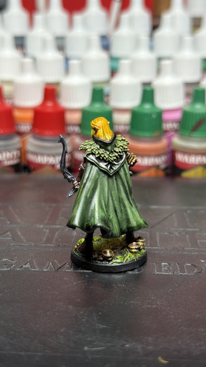 Rear view of the finished mini showing the weathered forest-green cape and metal bow